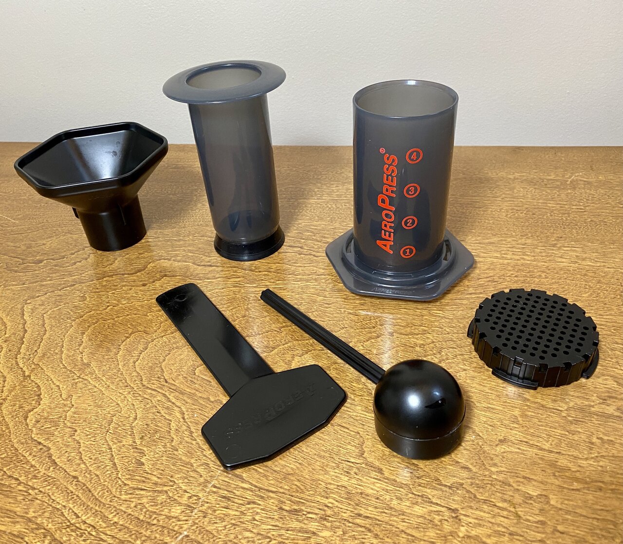 Classic gray AeroPress Original with red markings, separated plunger and older accessories on a wooden table