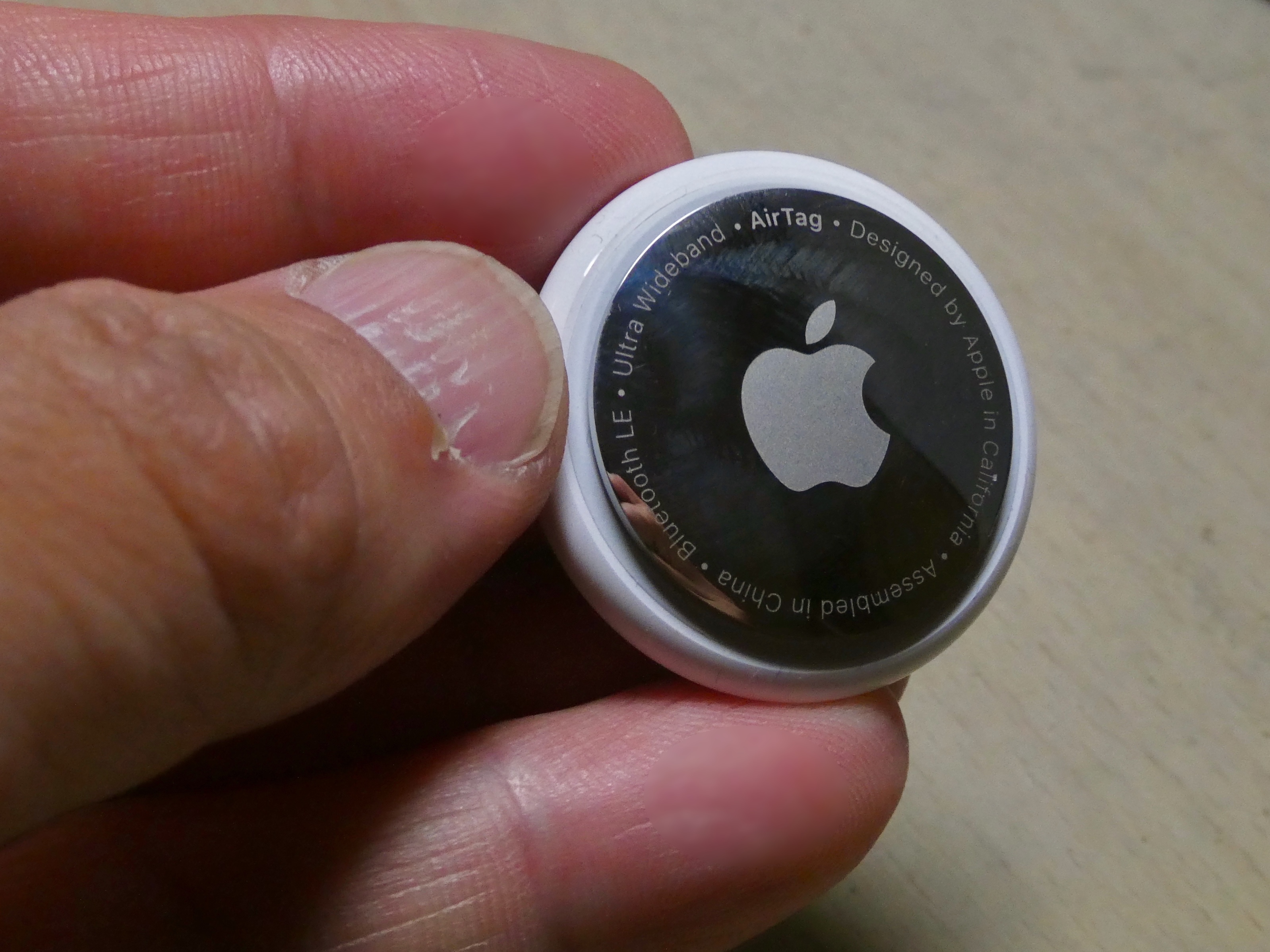A single first-generation Apple AirTag held in a hand with its metal back visible
